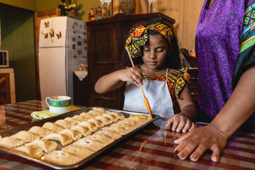 Horizontal de una niña afrocaribeña ayudando a su madre a preparar unos deliciosos bocadillos al estilo caribeño en el interior de su hogar. 