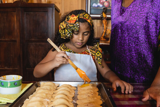 Horizontal de una ni&ntilde;a afrocaribe&ntilde;a ayudando a su madre a preparar unos deliciosos bocadillos al estilo caribe&ntilde;o en el interior de su hogar. 