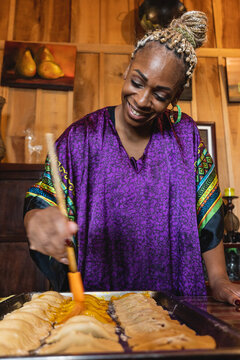 Imagen vertical de una mujer afrocaribe&ntilde;a muy sonriente en el interior de su casa preparando algunos bocadillos caribe&ntilde;os. 