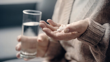 partial view of senior woman with dementia holding pills and glass of water.