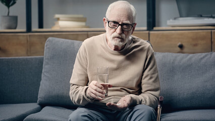 Fototapeta premium Senior man with dementia holding pills and glass of water.