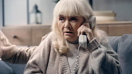 doubtful senior woman with dementia talking on telephone near husband.