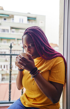 african american woman drinking coffee sitting at kitchen window