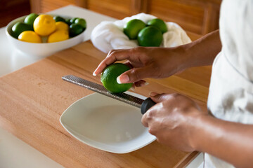 Obraz na płótnie Canvas African American woman, Black woman hands preparing to zest a lime with fine grater on a wooden cutting board