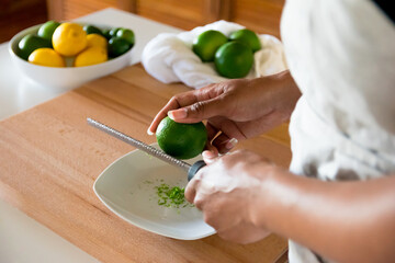 Obraz na płótnie Canvas African American woman, Black woman hands zesting a lime with fine grater on a wooden cutting board