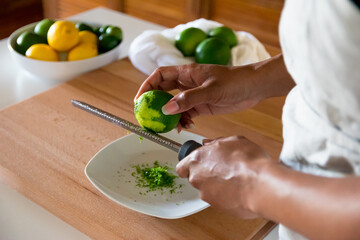 Obraz na płótnie Canvas Black woman, African American woman hands zesting a lime with fine grater on a wooden cutting board