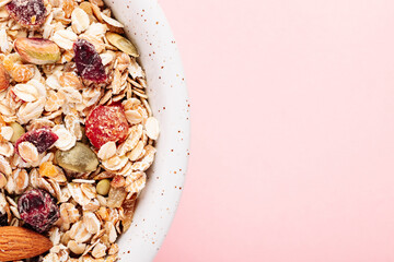 Oat muesli with nuts, dried berries and seeds in a bowl on a pink background close-up