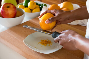 Black woman, African American woman hands zesting a orange with fine grater on a wooden cutting...