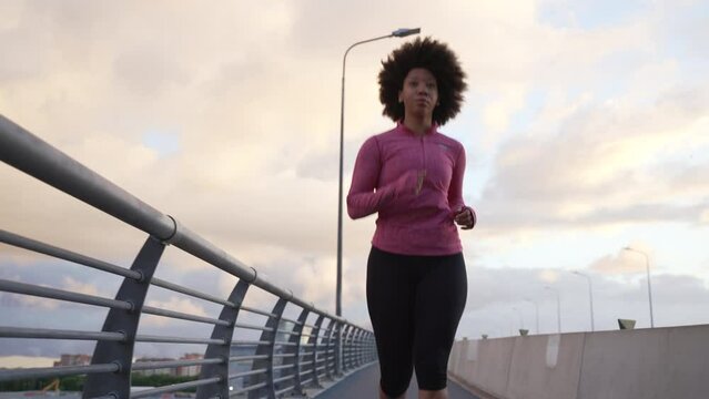 4k Young woman runner runs on bridge in city spbas. Portrait american african female athlete running and doing fit exercise with effort, working out and posing outdoors in summer. Beautiful active
