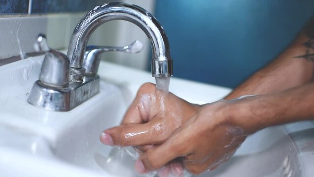 Hombre delgado caucasico lavandose las manos en un grifo de baño 