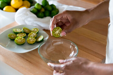 African American woman hands holding half cut shikuwasa Okinawa lime cross section above glass bowl