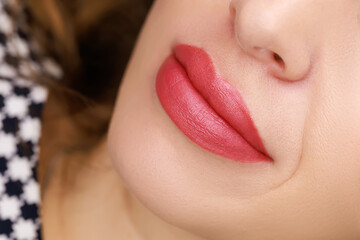 young model With a slight smile, on which permanent lip makeup is done with red pigment for...