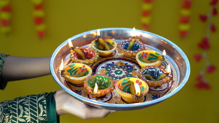 Indian woman or girl holding lit traditional clay diya or oil lamp with a thali or plate full of...