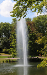 Naklejka premium high jet of water from the fountain in the middle of the pond in the park
