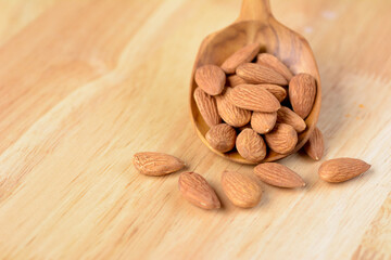 Almonds in wooden spoon against brown wooden background.