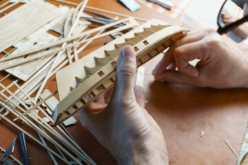 Hands of man gluing plywood details for ship model with glue, holding with fingers. Process of...