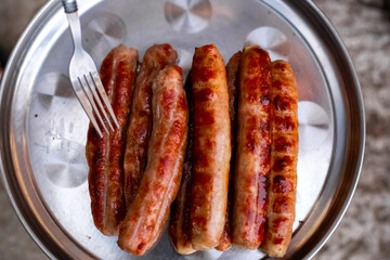 Grilled meat sausages on a metal dish. Delicious food at a weekend picnic.