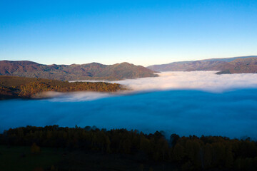 Fototapeta na wymiar Flying above the clouds in dawn. Misty morning in the valley, aerial view