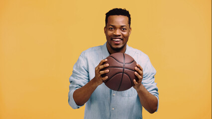 happy african american man holding basketball isolated on yellow.