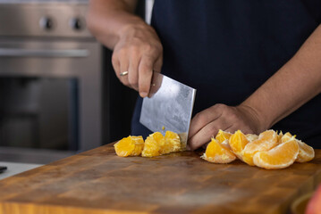 Chef cook cutting fresh orange for fruit salad on wooden cut board