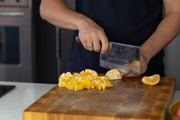 Chef cook cutting fresh orange for fruit salad on wooden cut board