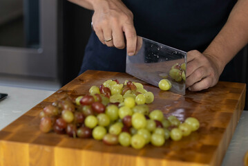 Chef cook cutting fresh grape for fruit salad on wooden cut board