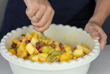 Chef cook mixing and making fresh healthy vegan Fruit Salad from orange, mango, apricot, pear, grape with drinking yogurt