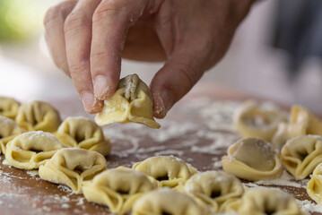 Chef cook hands making handmade Tortellini ravioli on wooden cut board with flour. Italian cuisine.