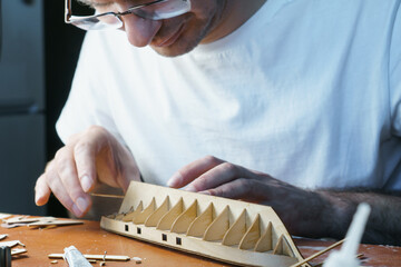 Hands of man gluing plywood details for ship model with glue, holding with fingers. Process of...