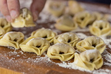 Chef cook hands making handmade Tortellini ravioli on wooden cut board with flour. Italian cuisine.