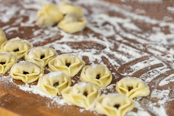 Fototapeta na wymiar Chef cook hands making handmade Tortellini ravioli on wooden cut board with flour. Italian cuisine.