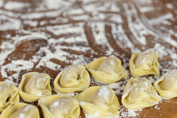 Chef cook hands making handmade Tortellini ravioli on wooden cut board with flour. Italian cuisine.