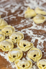 Chef cook hands making handmade Tortellini ravioli on wooden cut board with flour. Italian cuisine.