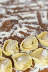 Chef cook hands making handmade Tortellini ravioli on wooden cut board with flour. Italian cuisine.