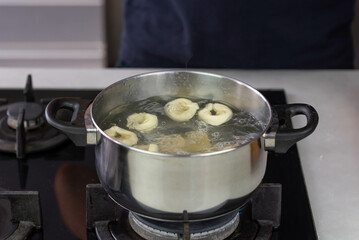 Chef cook hand making handmade tortellini ravioli with boiling water in pot saucepan on stove fire.