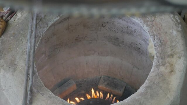 Top view baker's hand glues dough to hot tonir for baking national bread in stone tundyr. Delicious fragrant crispy puri and matnakash. Baking traditional bread