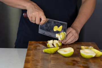 Chef cook cutting fresh pear for fruit salad on wooden cut board