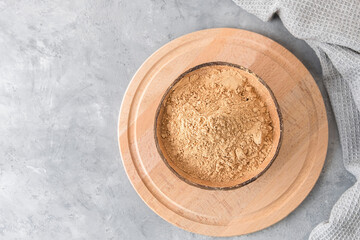 Top view of a bowl with raw maca root powder on light grey background with copy space