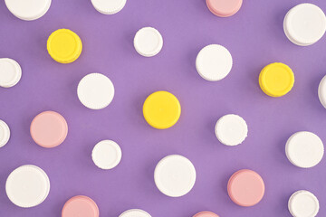 Top view of white, yellow and pink plastic bottle caps, in a chaotic pattern on purple background