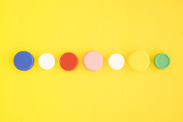 Top view of colorful plastic bottle caps lined up on yellow background