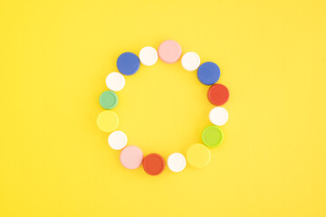 Top view of multicolored plastic bottle caps arranged in circle on yellow background