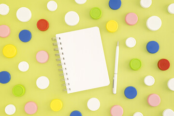 Top view of white notepad and colorful plastic bottle caps on green background