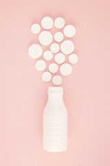 Top view of white plastic bottle and caps on pink background