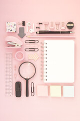 Flat lay of desk mockup concept: notepad, headphones, magnifier and stationery on pink background