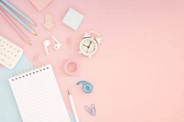 Flat lay of desk mockup concept: notepad, clock, headphones and stationery on pink and blue background