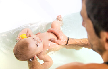 The father bathes the baby in the bath. Selective focus.