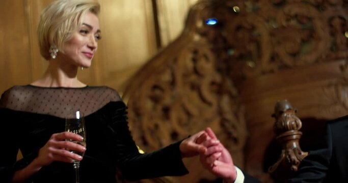 Happy bearded man in suit giving hand to his charming woman in elegant evening dress walking down stairs at luxury hotel. Lovely couple of celebrity in casino.