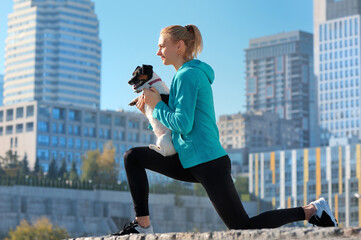 Woman making lunge exercise holding dog in hands