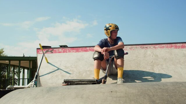 Portrait of man with kick scooter in concrete bowl, air extreme skate park, young skater sweating after training boy. 