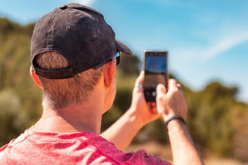 Man in cap photographing the natural landscape with his smartphone.